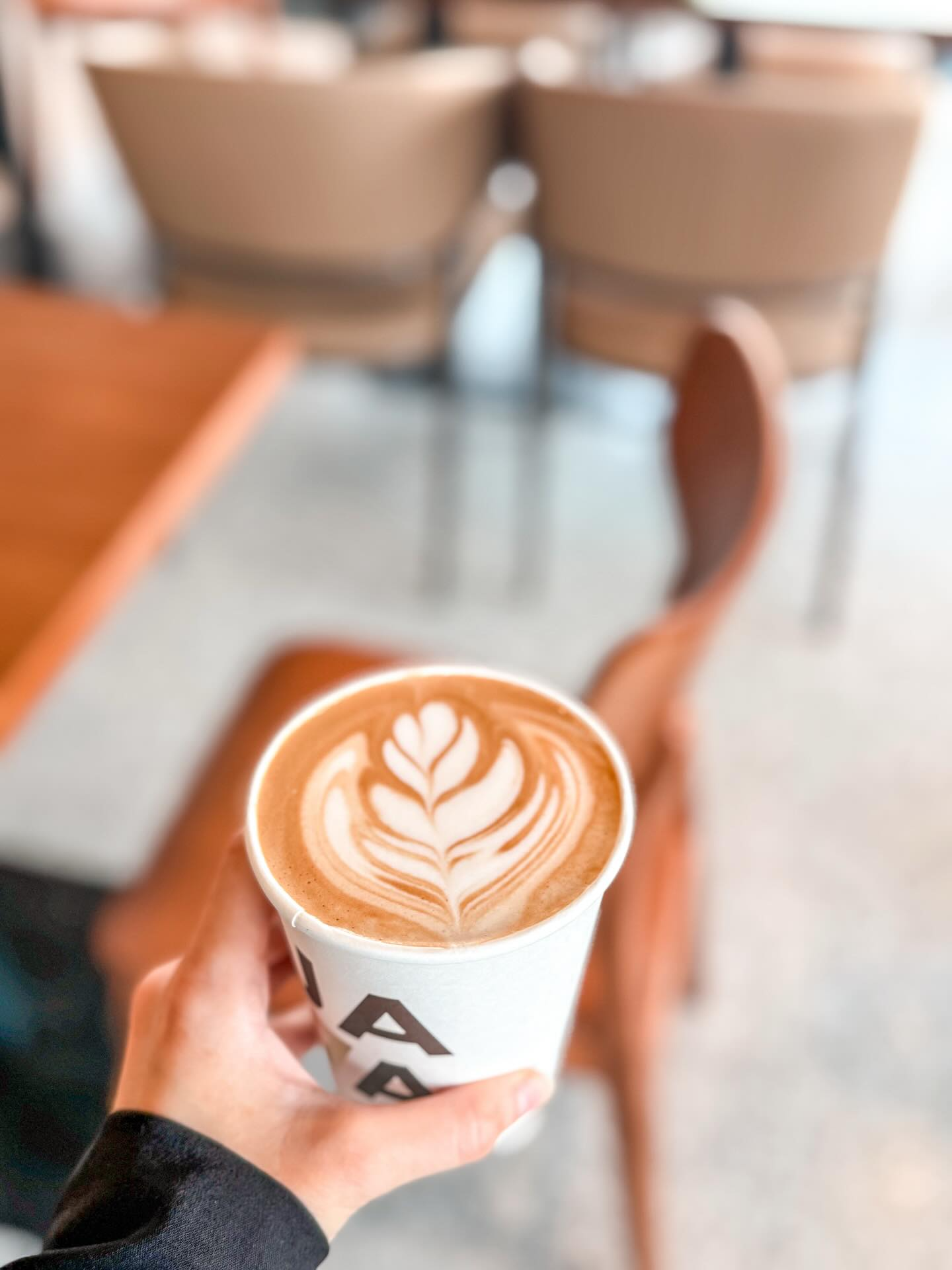A latte with leaf art being held inside a cafe